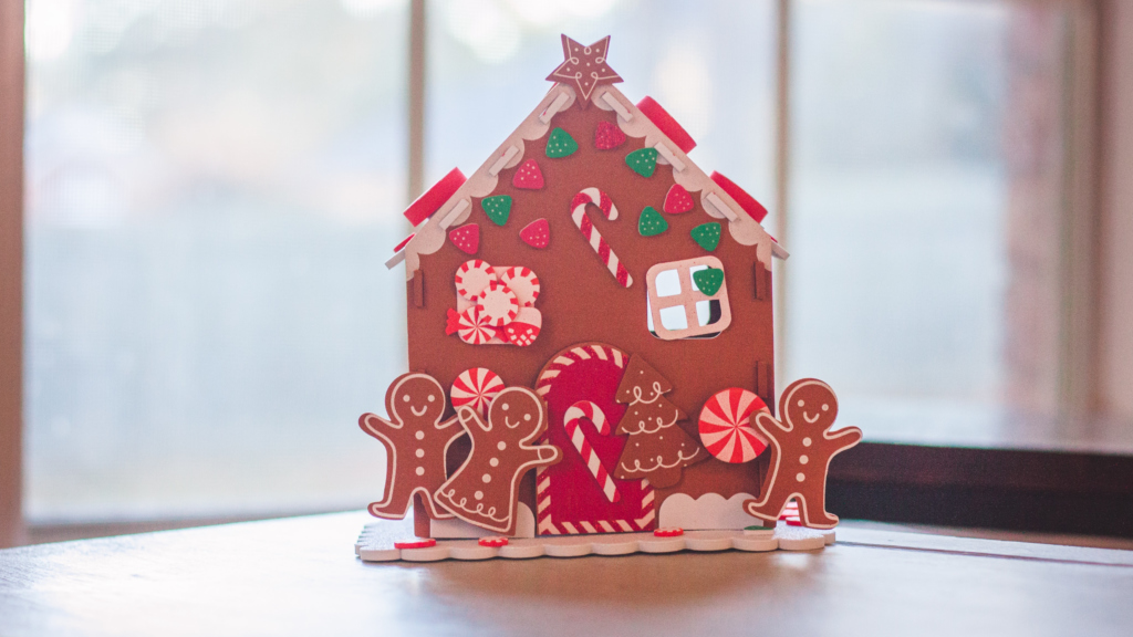 Gingerbread house sitting on a table infront of a window.